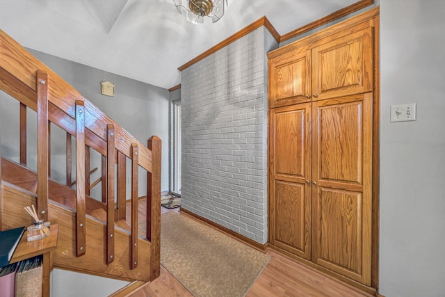 interior space with brick wall, ornamental molding, and light wood-style floors