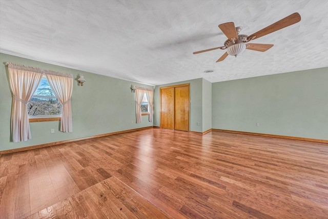 empty room featuring a wealth of natural light, a textured ceiling, baseboards, and wood finished floors