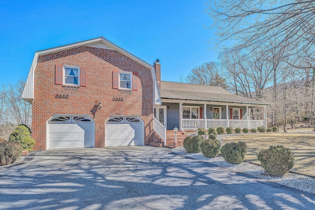 tri-level home with brick siding, a chimney, a porch, a garage, and driveway