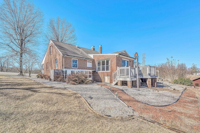 back of house featuring brick siding, a chimney, a wooden deck, and stairs