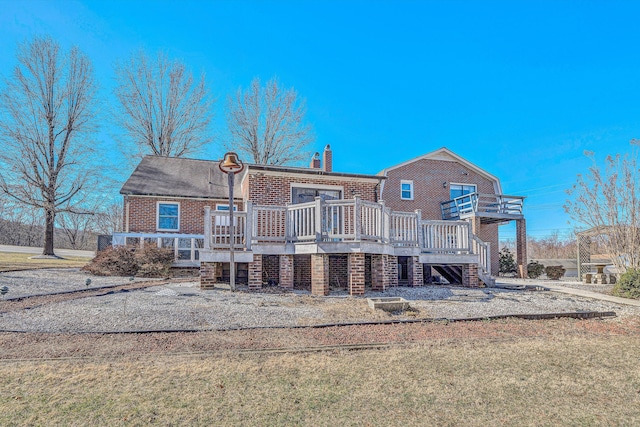 rear view of house with a deck, brick siding, a chimney, and stairs