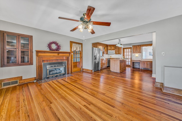 unfurnished living room with a fireplace with flush hearth, visible vents, baseboards, and wood finished floors