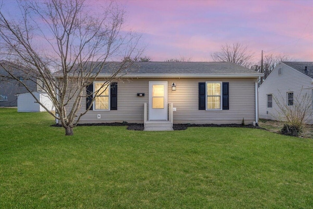 view of front of property with a shingled roof and a lawn