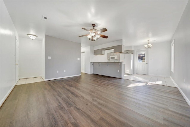 unfurnished living room with light wood-type flooring, visible vents, baseboards, and ceiling fan with notable chandelier