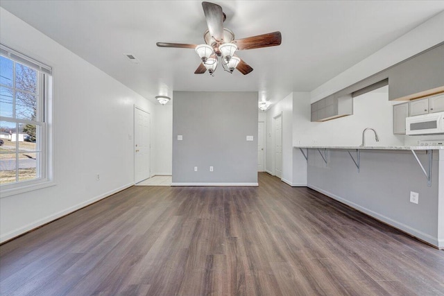 unfurnished living room with visible vents, dark wood-type flooring, a ceiling fan, a sink, and baseboards