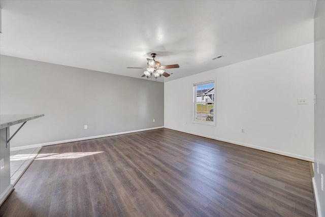 empty room with dark wood-type flooring, visible vents, ceiling fan, and baseboards