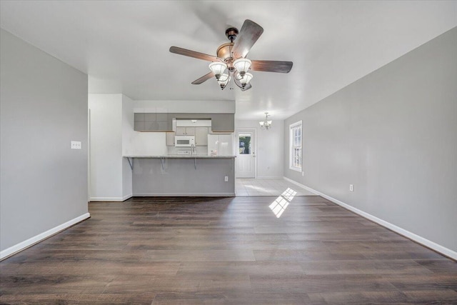 unfurnished living room with ceiling fan with notable chandelier, baseboards, and wood finished floors