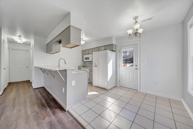 kitchen featuring a peninsula, white appliances, a sink, visible vents, and a kitchen bar