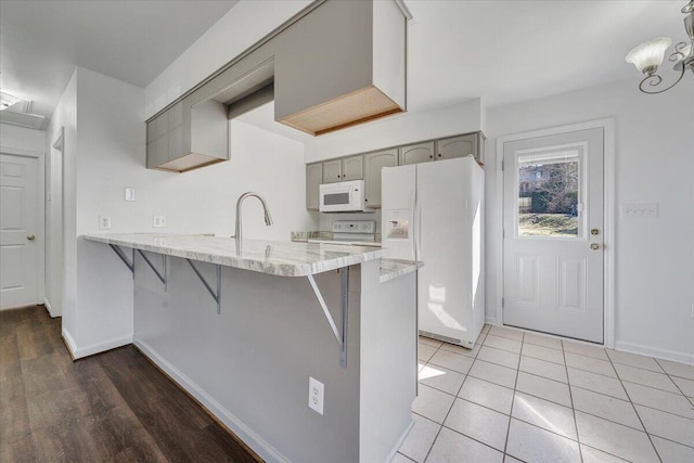 kitchen featuring a kitchen bar, gray cabinets, white appliances, a peninsula, and baseboards