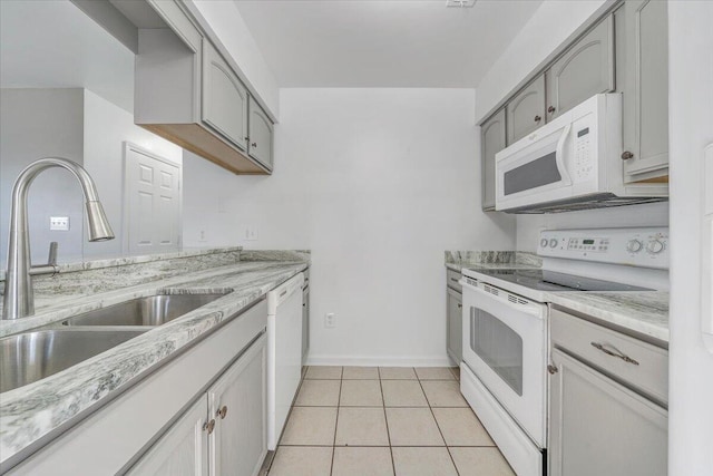 kitchen featuring white appliances, light tile patterned floors, baseboards, light stone counters, and a sink