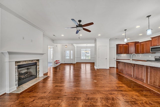 kitchen featuring a stone fireplace, stainless steel appliances, backsplash, brown cabinets, and dark wood-style floors