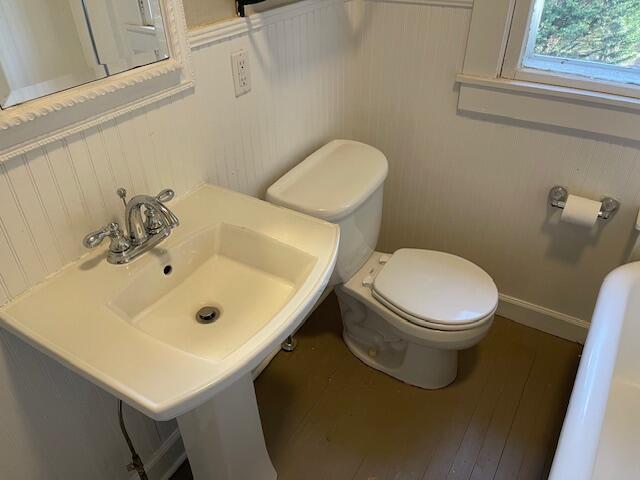 half bath with baseboards, toilet, and wood finished floors