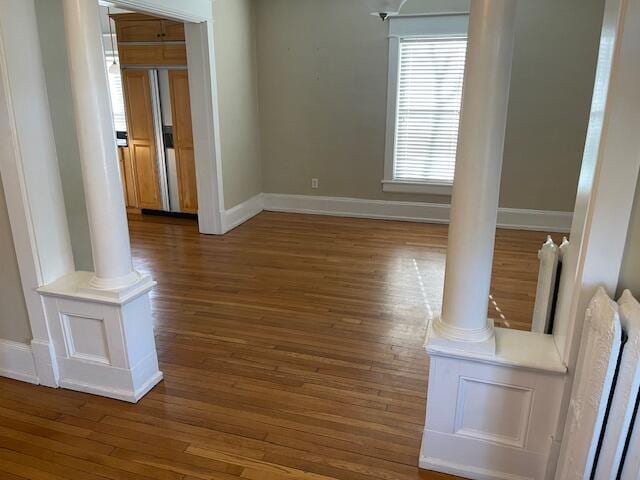 unfurnished room with decorative columns, baseboards, and wood finished floors