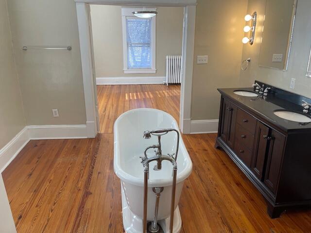 bathroom featuring radiator heating unit, a freestanding bath, a sink, and wood finished floors