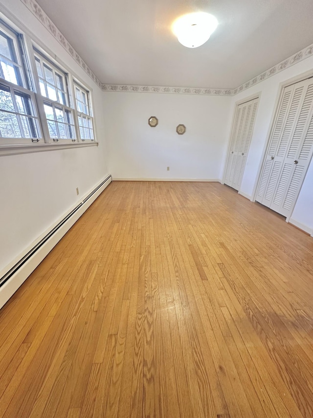 spare room with a baseboard heating unit, light wood-type flooring, and baseboards