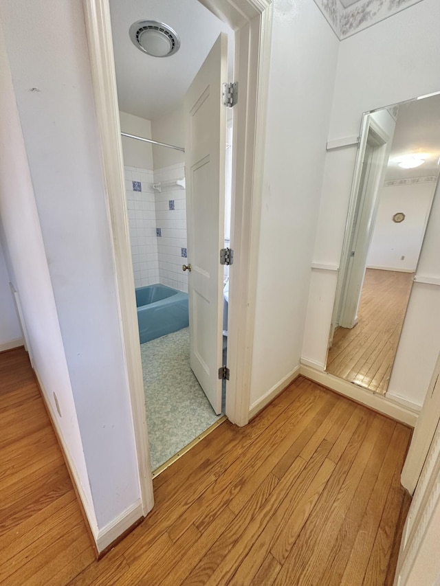 hall with baseboards, visible vents, and wood finished floors