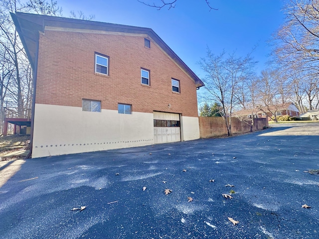 view of side of home with an attached garage, fence, aphalt driveway, and brick siding