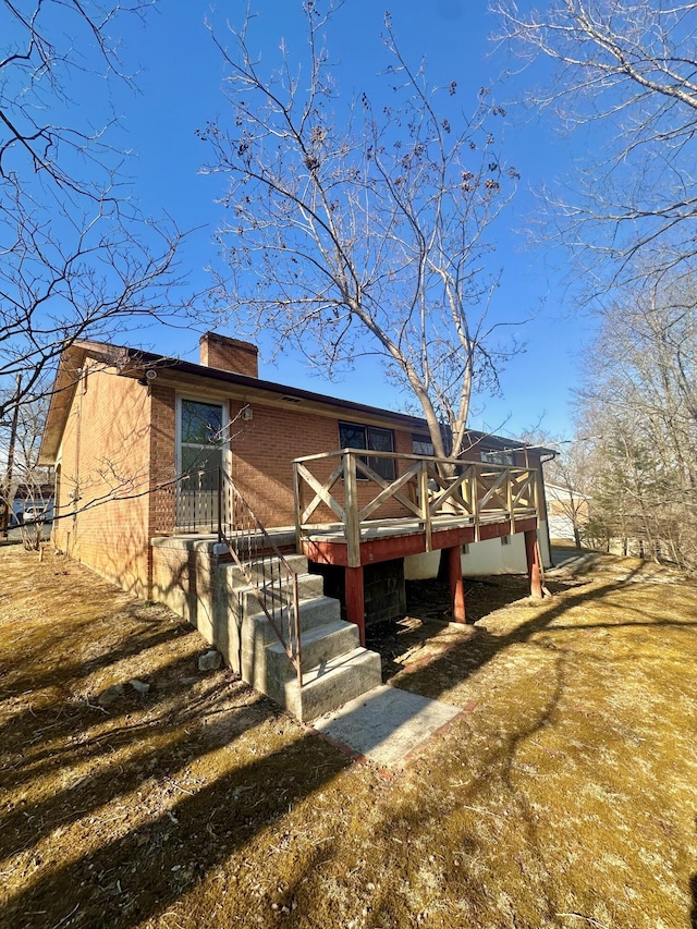 view of front of house with stairway, brick siding, a chimney, and a wooden deck