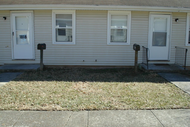 entrance to property with a shingled roof and a yard