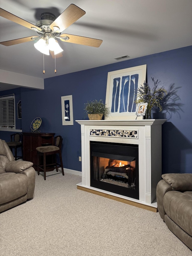 living area featuring visible vents, a ceiling fan, carpet floors, a lit fireplace, and baseboards