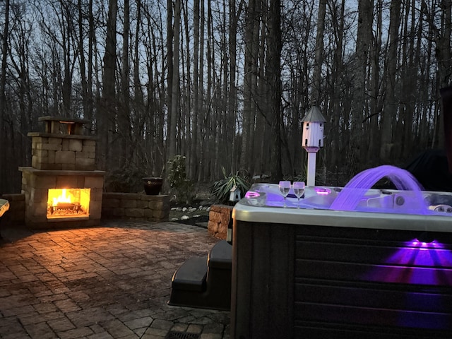 view of patio with a warm lit fireplace and a hot tub