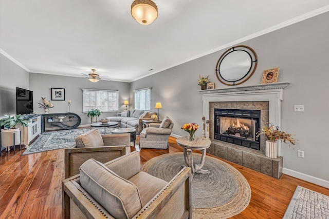 living room with ornamental molding, wood finished floors, a fireplace, baseboards, and ceiling fan