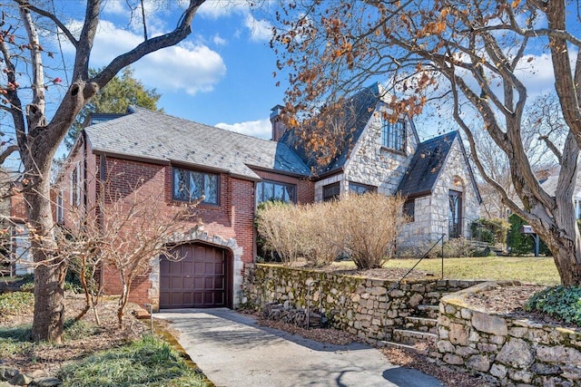 english style home featuring brick siding, a chimney, a garage, a high end roof, and driveway