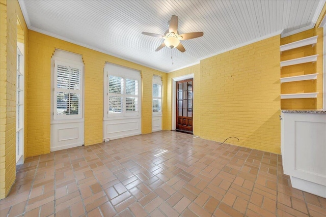 spare room with brick floor, crown molding, ceiling fan, and brick wall