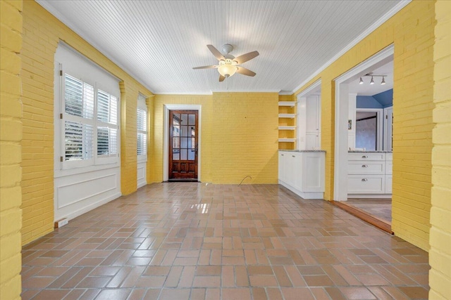 spare room featuring ceiling fan, brick wall, and brick floor