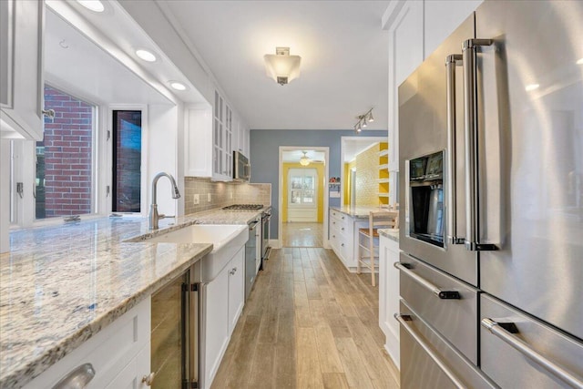 kitchen featuring wine cooler, stainless steel appliances, white cabinetry, light wood-style floors, and backsplash