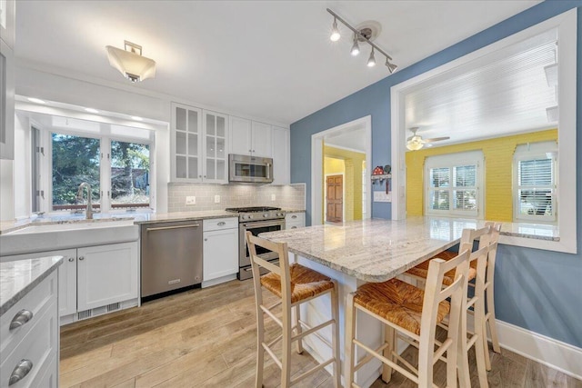 kitchen featuring white cabinets, glass insert cabinets, a kitchen breakfast bar, stainless steel appliances, and light wood-type flooring