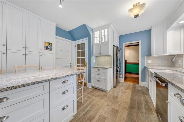 kitchen with light wood-style flooring, stainless steel appliances, a sink, white cabinets, and decorative backsplash