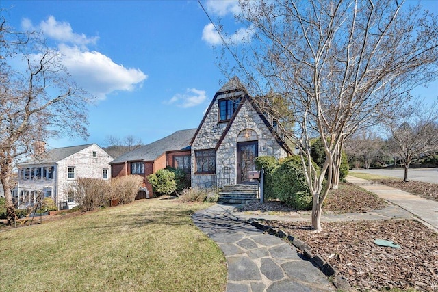 tudor house featuring stone siding, brick siding, and a front yard