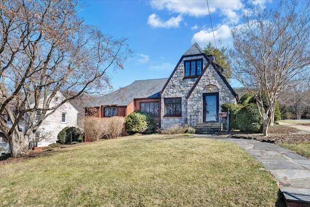 tudor home featuring stone siding, brick siding, and a front yard