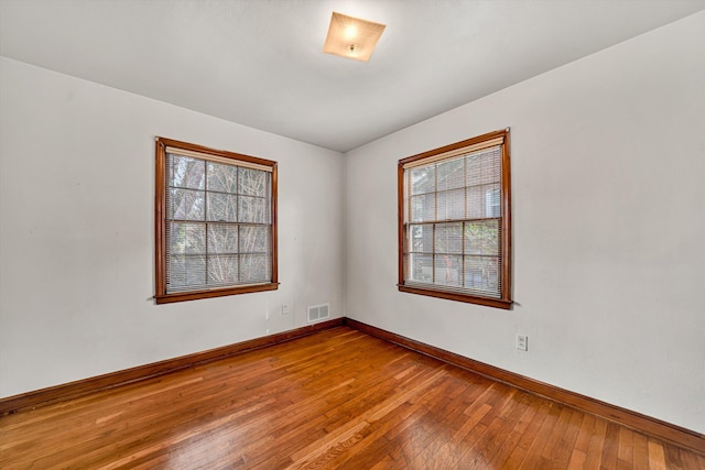 empty room with visible vents, baseboards, and hardwood / wood-style flooring