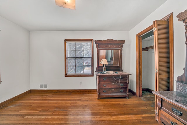 bedroom with hardwood / wood-style floors, baseboards, visible vents, and a closet