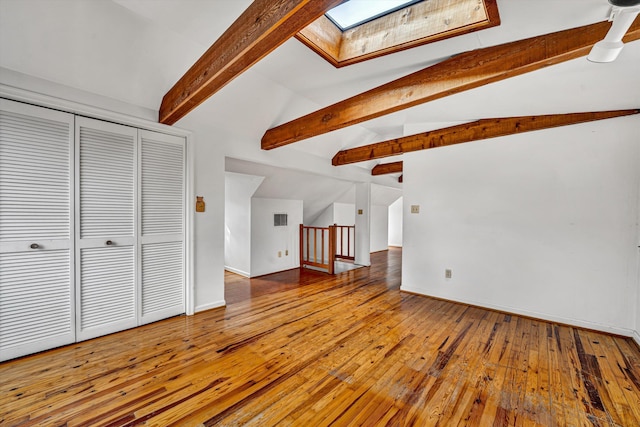 unfurnished living room featuring visible vents, vaulted ceiling with skylight, baseboards, and wood-type flooring