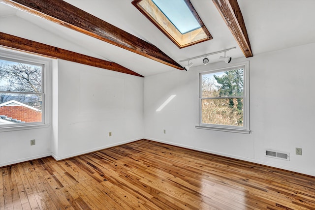 empty room featuring visible vents, track lighting, baseboards, lofted ceiling with skylight, and hardwood / wood-style flooring