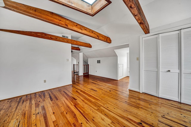 unfurnished living room with lofted ceiling with skylight, visible vents, light wood finished floors, and baseboards