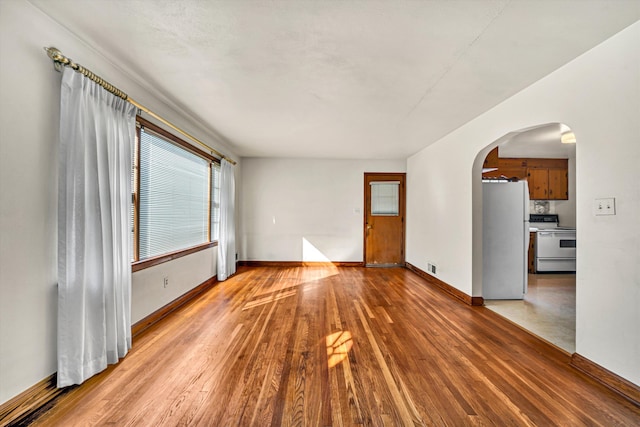 unfurnished room featuring baseboards, arched walkways, and light wood finished floors