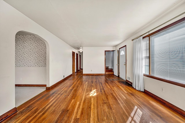 spare room featuring arched walkways, visible vents, baseboards, and hardwood / wood-style flooring