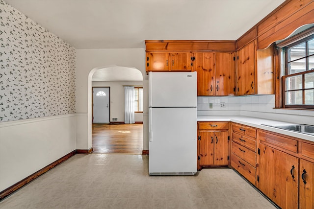 kitchen featuring arched walkways, brown cabinetry, light countertops, and freestanding refrigerator