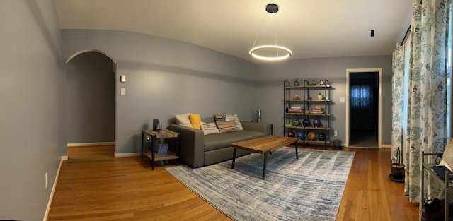 sitting room with arched walkways, vaulted ceiling, light wood-style flooring, and baseboards