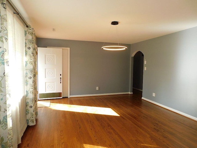 empty room featuring baseboards, arched walkways, and wood finished floors