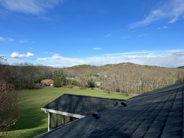 exterior space featuring roof with shingles and a wooded view