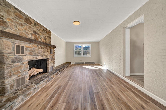 unfurnished living room featuring a baseboard radiator, visible vents, wood finished floors, and a stone fireplace