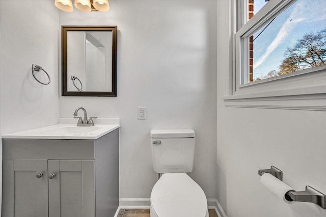 half bath with baseboards, vanity, and toilet