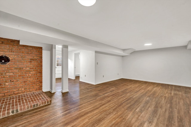 finished below grade area featuring brick wall, baseboards, and wood finished floors