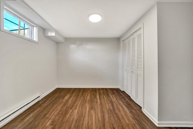 basement with a baseboard heating unit, dark wood-type flooring, and baseboards