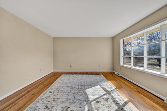 empty room featuring wood finished floors, visible vents, and baseboards